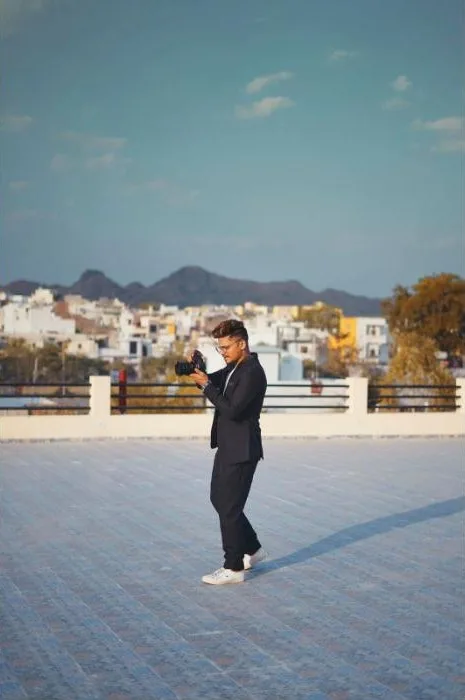 Avi Jaiswal photographing on a rooftop with a city and hills behind